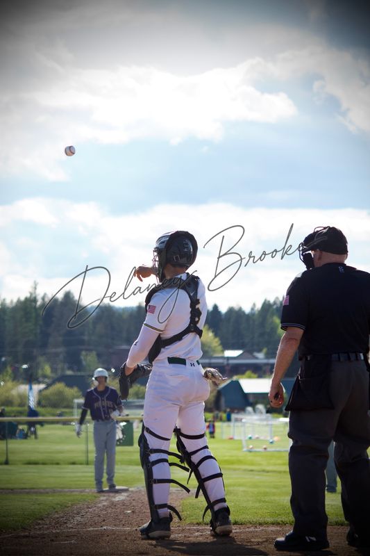 A baseball catcher tracking a pop-up into the sky, the umpire standing beside him.