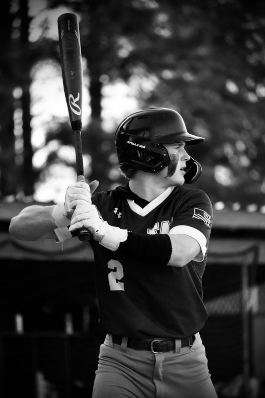 A baseball batter waiting for the pitch in black and white, bat raised behind his shoulder.