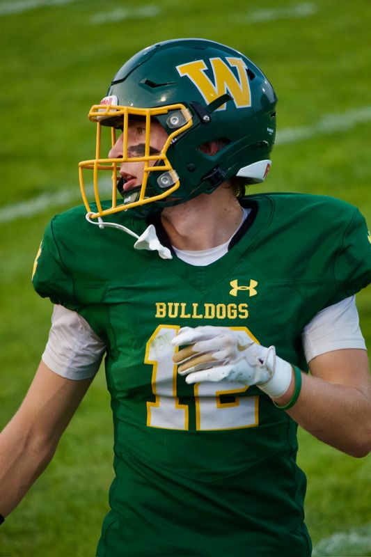 A football player in a green helmet and Bulldogs jersey looking off to the side, his mouthguard hanging loose.