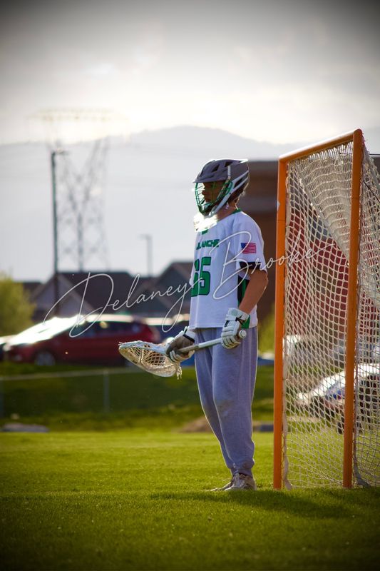 A lacrosse goalkeeper waiting beside the open goal, his stick held low.