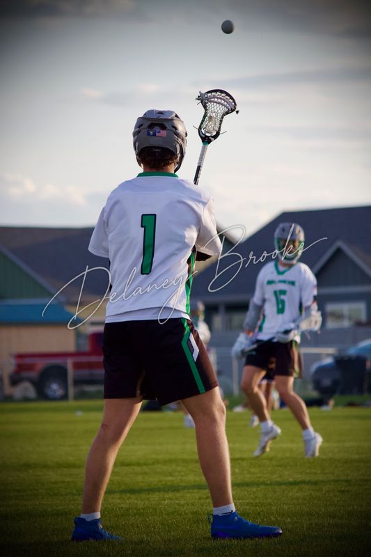 A lacrosse player reaching his stick up for a pass, the ball still in the air above him.