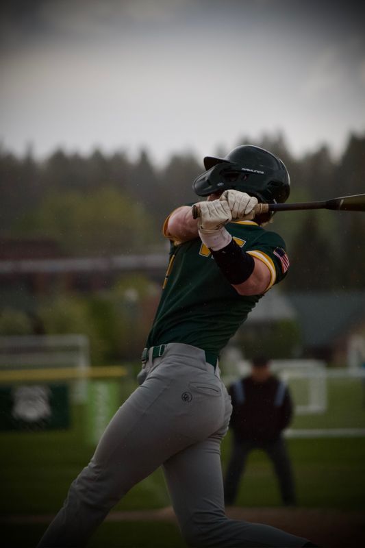 A baseball batter following through on a swing in the rain, water streaking the air around him.