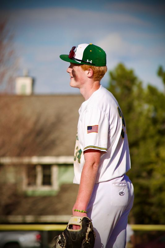 A baseball player standing in profile with his glove at his side, warm light across his face.