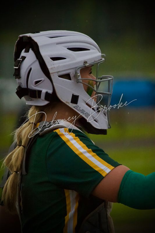 A softball catcher in profile wearing a white mask, in the rain.