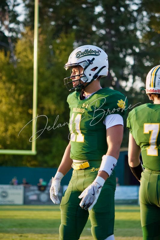 A football player in a white Bulldogs helmet standing on the field in warm evening light, a teammate beside him.