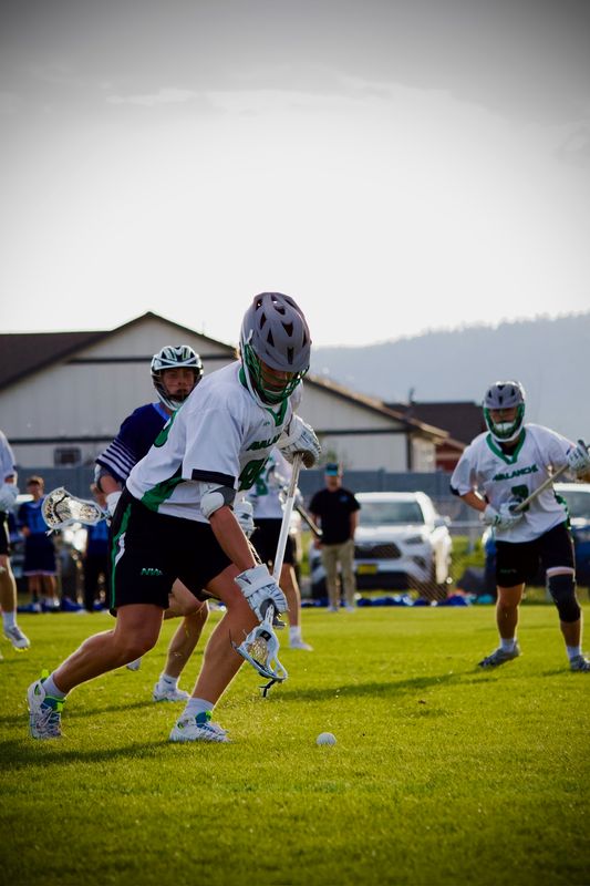 A lacrosse player bending for a ground ball, backlit by low sun.