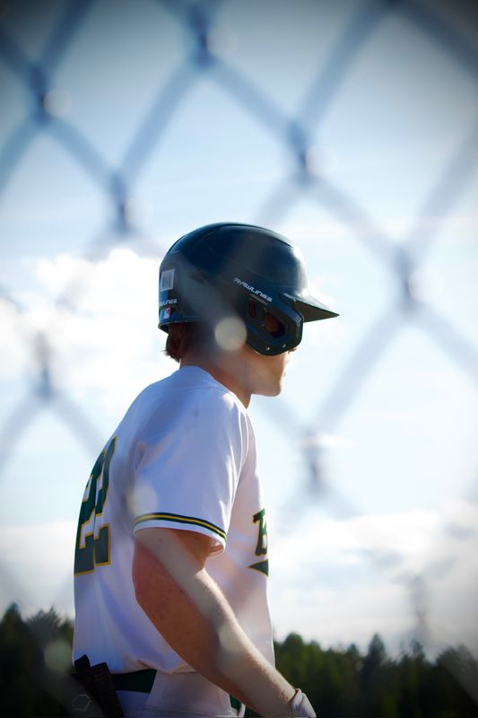 A baseball player photographed through the diamond of a chain-link fence.