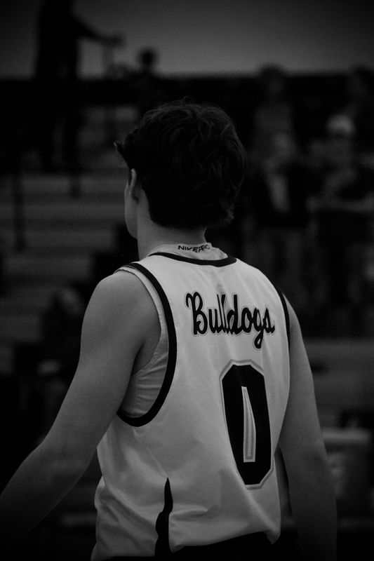 A basketball player seen from behind in a dim gym, in black and white.