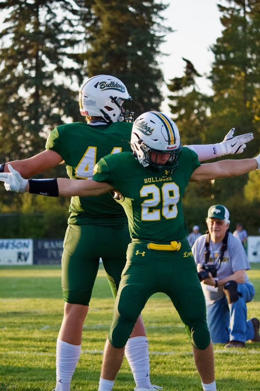 Two football players celebrating back to back with arms outstretched in low evening light, a photographer kneeling behind them.